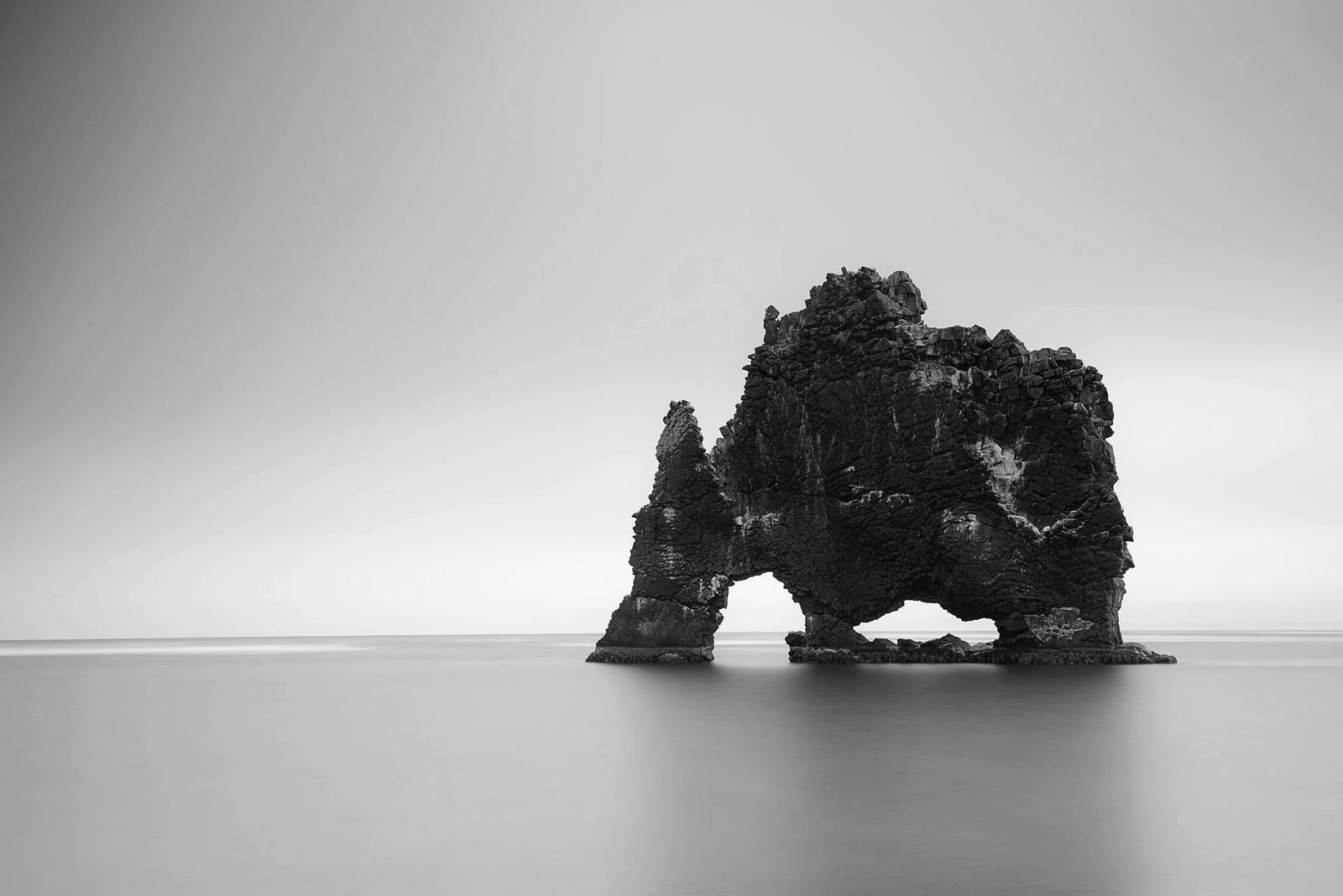 A lone basalt sea arch standing in still, grey water.